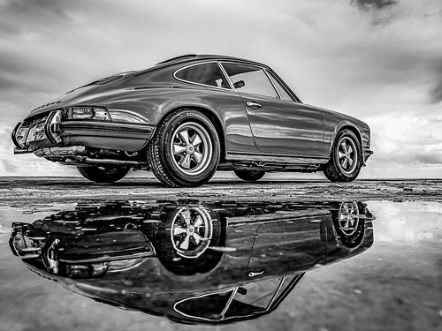 Photographie d'une voiture de collection, une Porsche 911 version noir et blanc, prise sur le Bassin d'Arcachon. Elle est captée avec son reflet dans une flaque d'eau. C'est une magnifique voiture vintage.