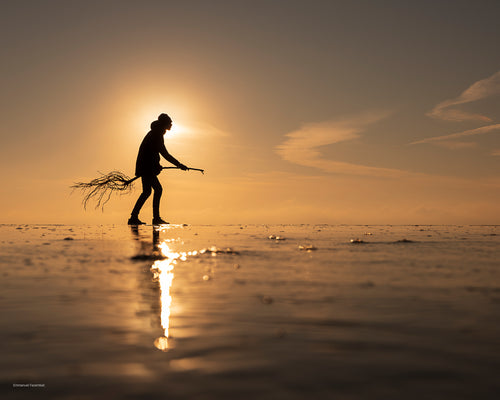 Photographie prise à la pointe du Cap-Ferret représentant la silhouette d'un homme sur un bout de bois ressemblant à un sorcier sur son balais. La photo est faite sur la plage au coucher de soleil.