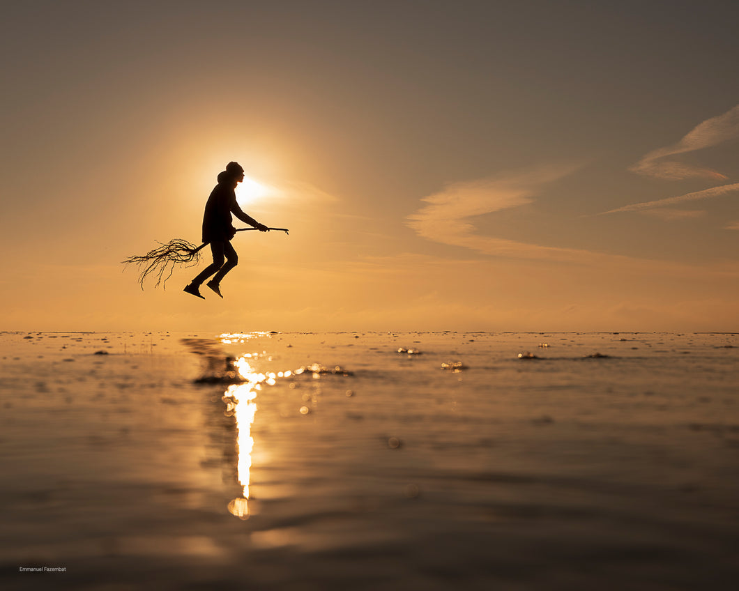 Photographie prise à la pointe du Cap-Ferret représentant la silhouette d'un homme sur un bout de bois ressemblant à un sorcier sur son balais. La photo est faite sur la plage au coucher de soleil.
